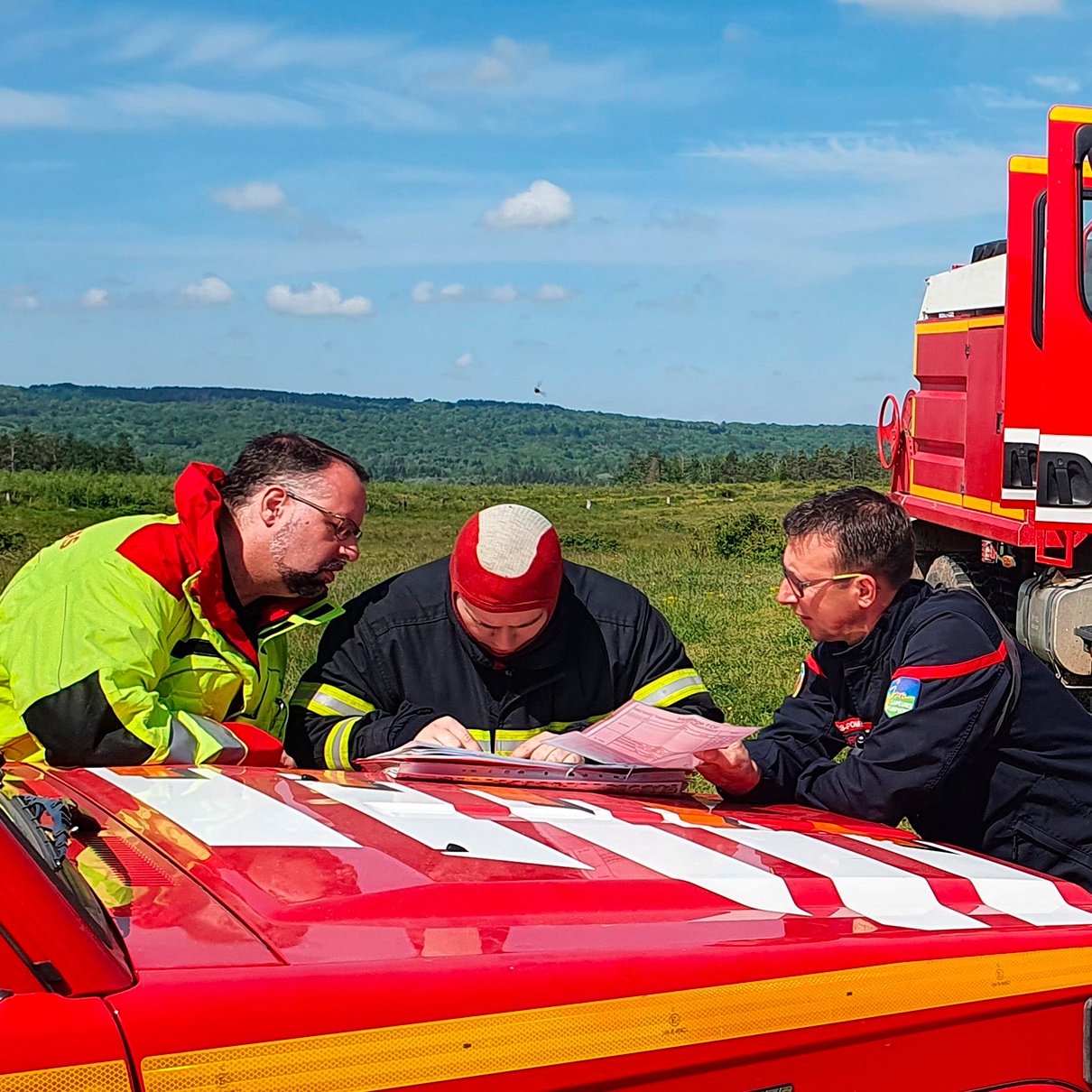 trois pompiers discutant autour d'un véhicule de pompier